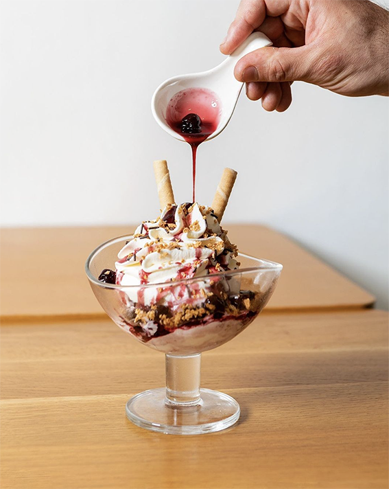 Ein üppig garnierter Eisbecher von Vanella Wien, serviert mit frischen Beeren, Schlagobers und Waffelröllchen, verfeinert mit einem Guss aus roter Fruchtsauce