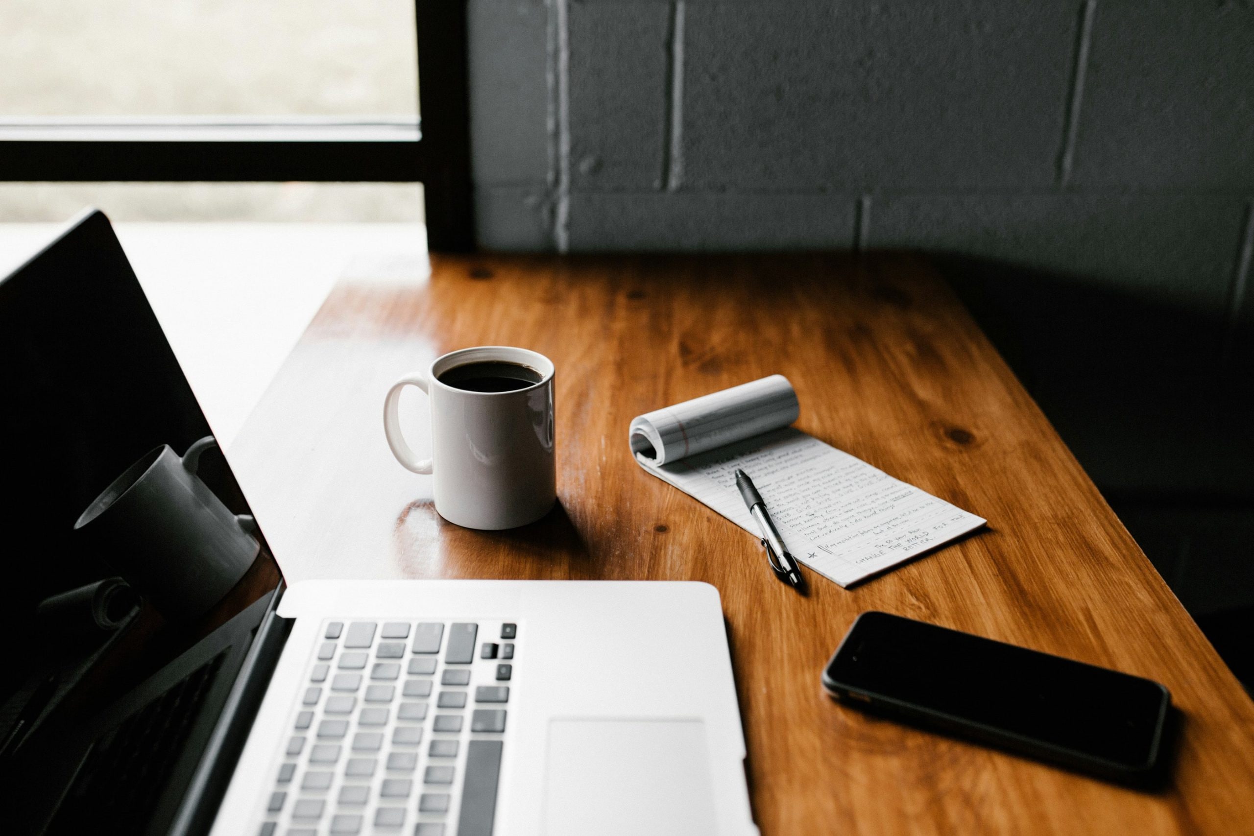 Schreibtisch mit Laptop, Smartphone, Kaffeetasse und Block mit Stift