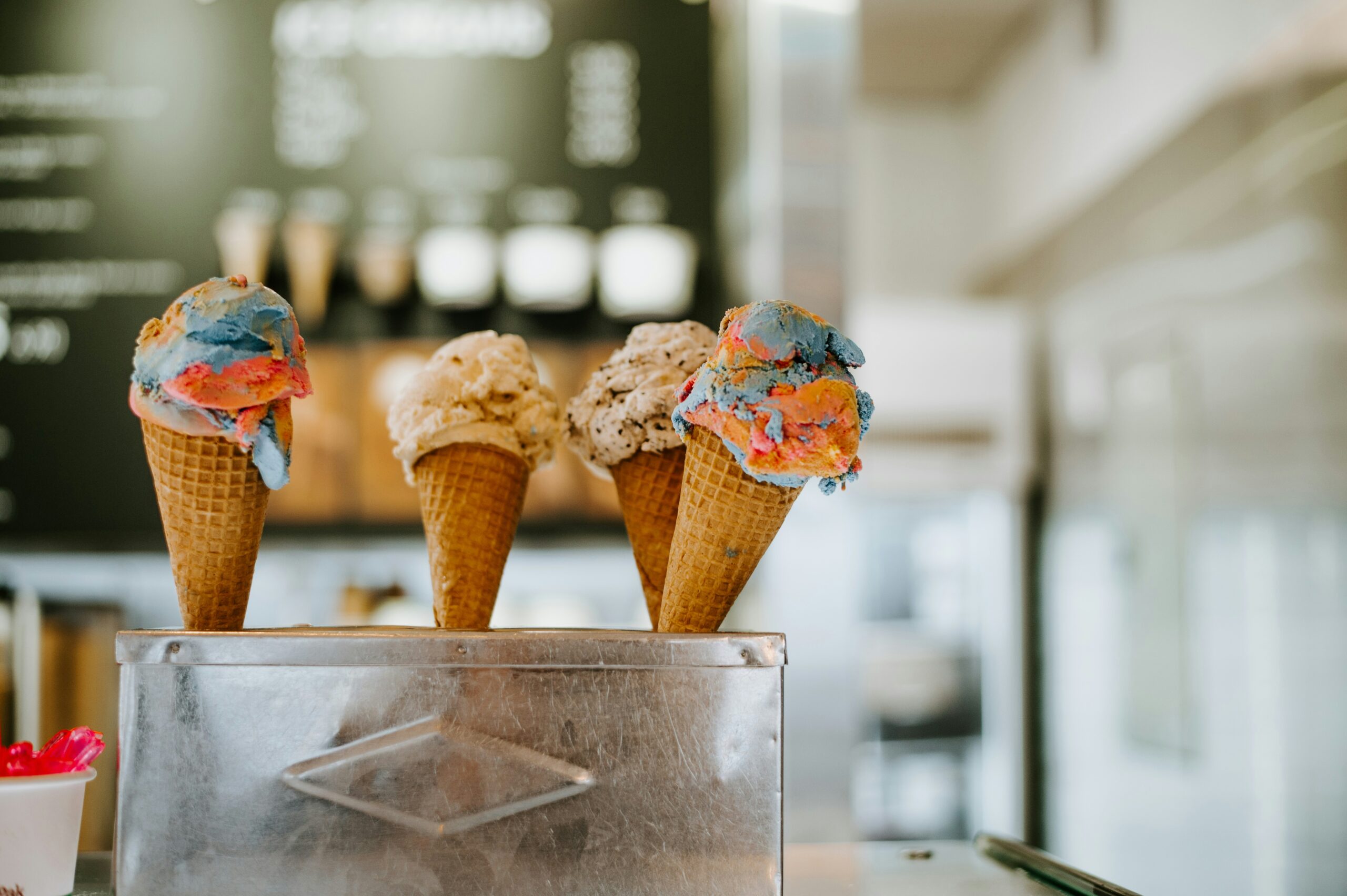 Drei Stanizel mit köstlichem, buntem Eis aus einem der besten Eissalons in Wien, präsentiert in einem metallenen Halter mit unscharfem Menü im Hintergrund