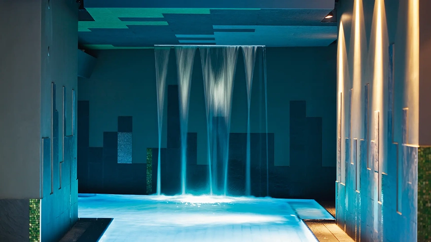 Moderne Wasserfall-Duschen beleuchtet in beruhigendem Blau in der Wellnessoase der Therme Wien Oberlaa